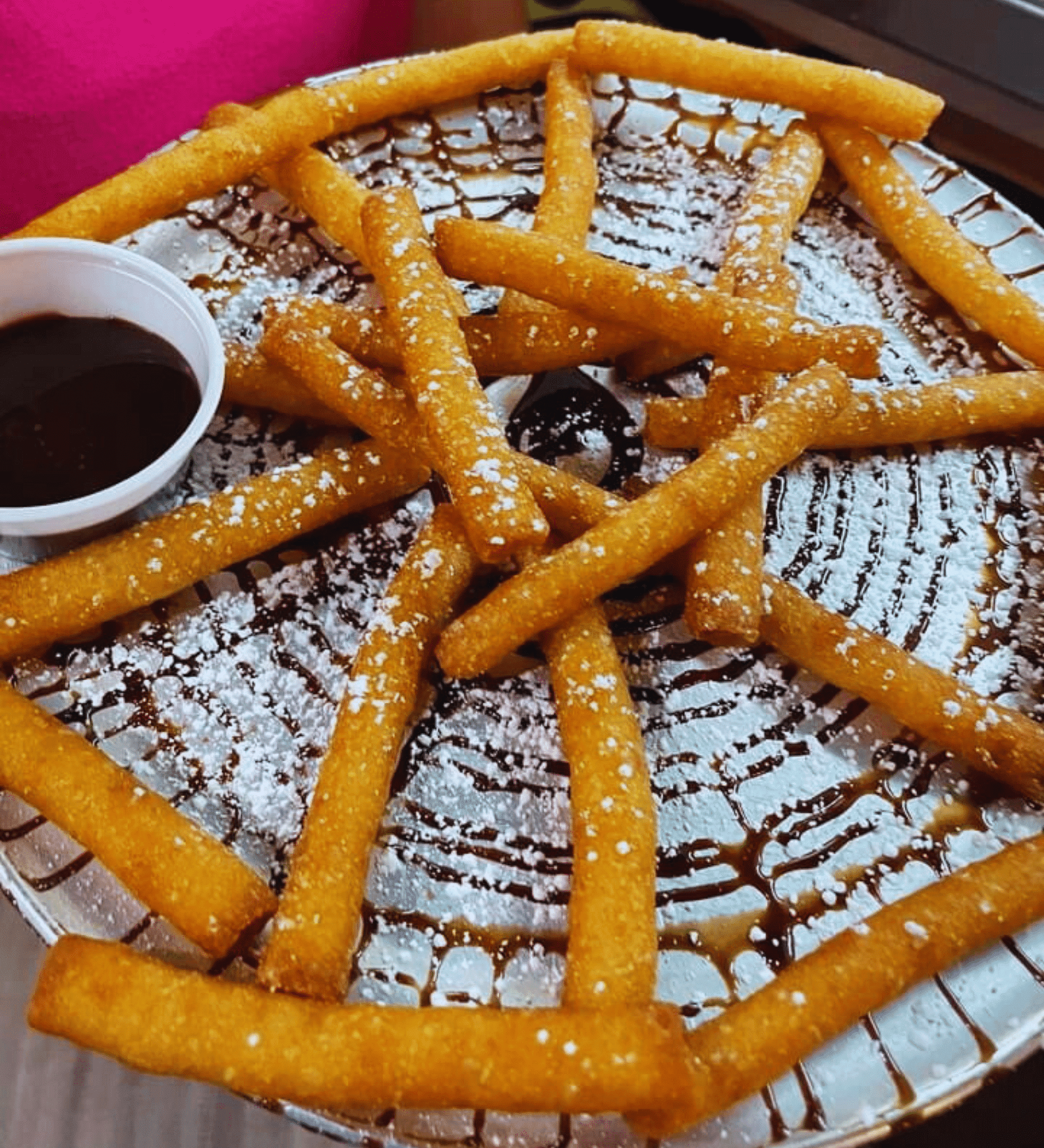 A plate of churros with sugar dusting and chocolate dipping sauce.